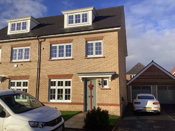 A three-storey brick new-build house with cars on the driveway