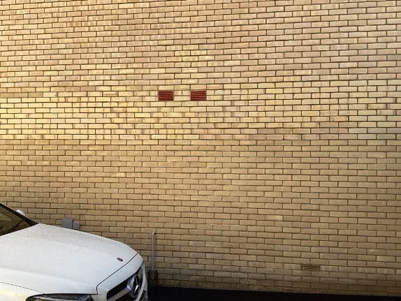 Cream brickwork with two weep vents above a parked car