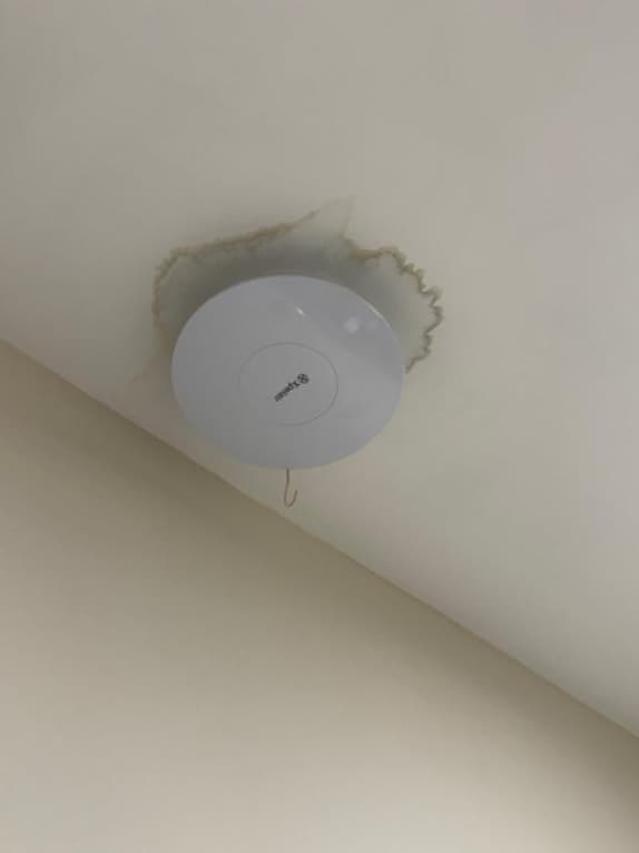 A ceiling-mounted smoke alarm with damaged plaster around it